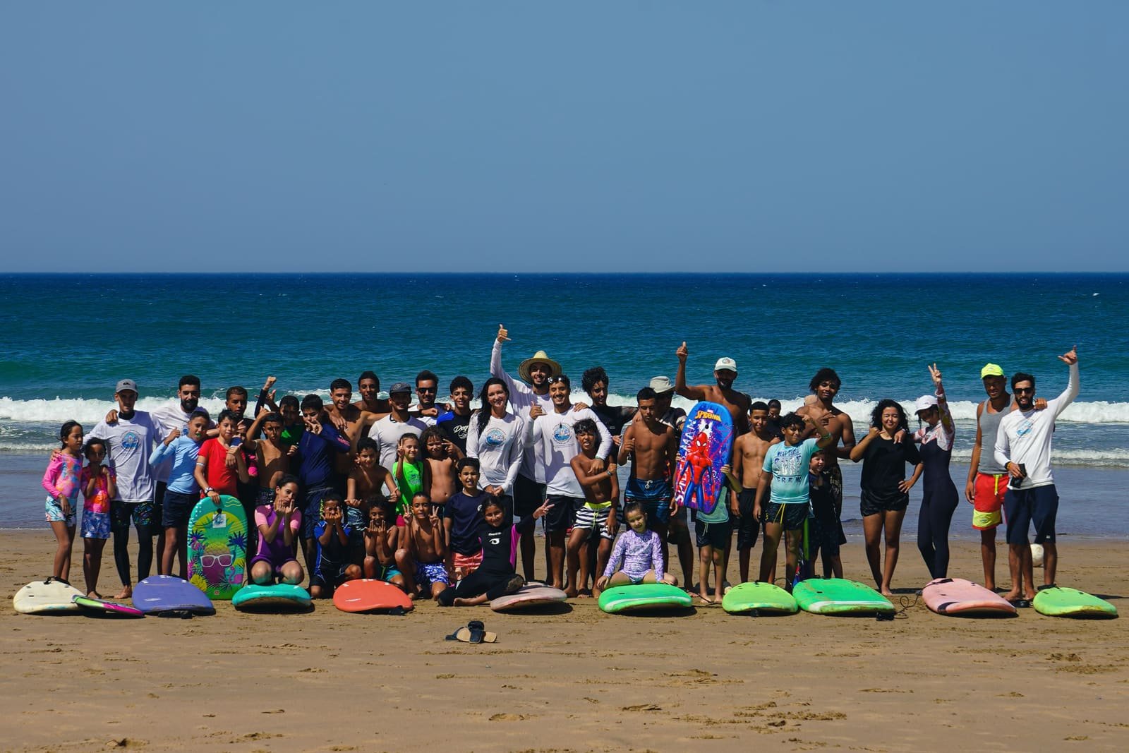 Kids, families, instructors and volunteers cheering behind a row of surfboards at the opening of the Surfboard Library in Asilah