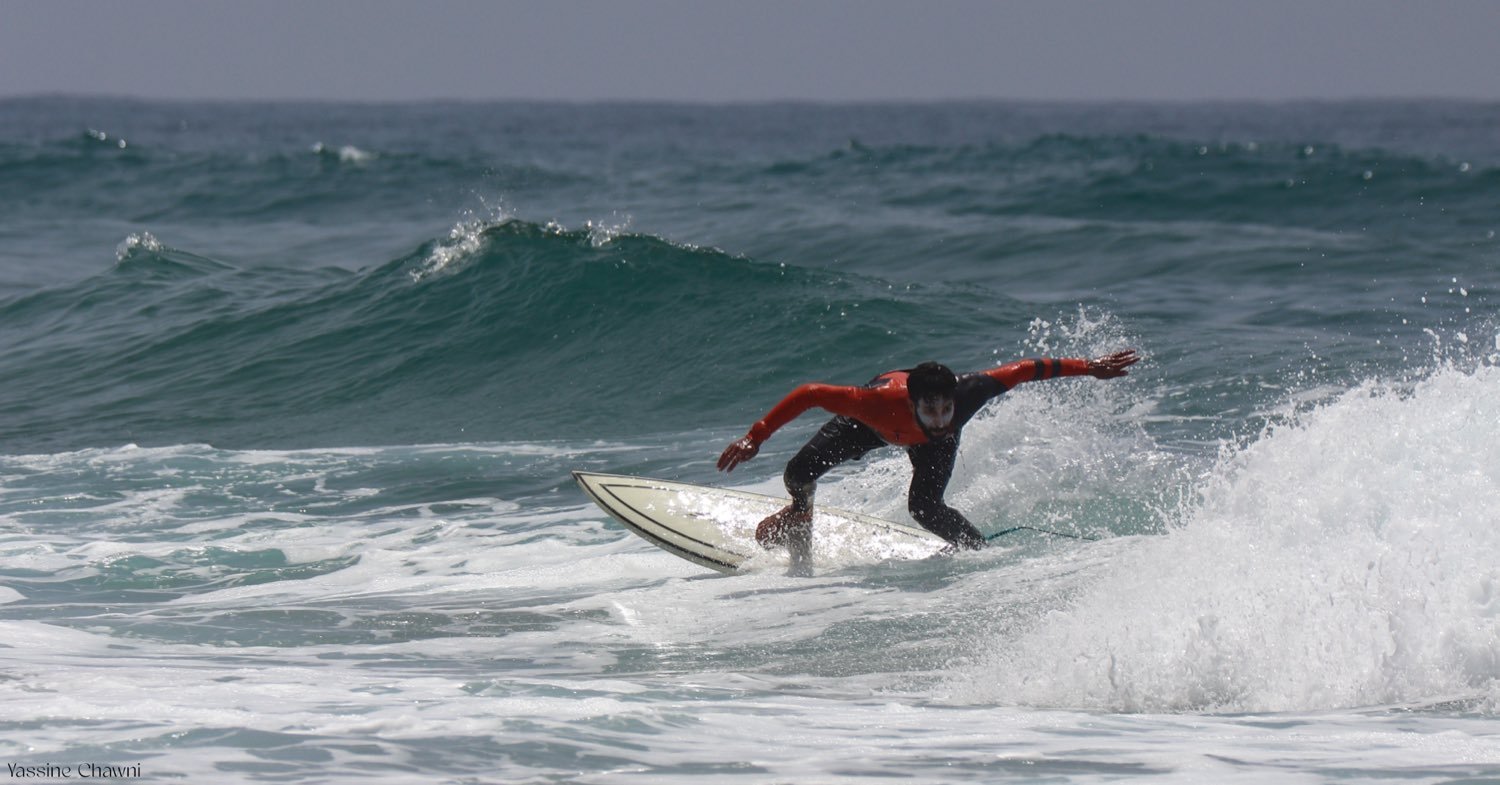 A surfer in a red and black wetsuit driving off the bottom of a wave